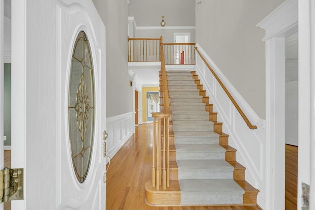 entryway with a decorative wall, a wainscoted wall, wood finished floors, a towering ceiling, and crown molding