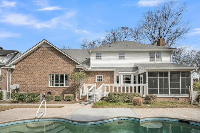 back of property with an outdoor pool, a sunroom, a chimney, a deck, and brick siding