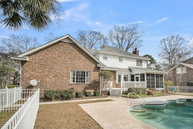 rear view of house with a sunroom, a patio area, brick siding, and a chimney