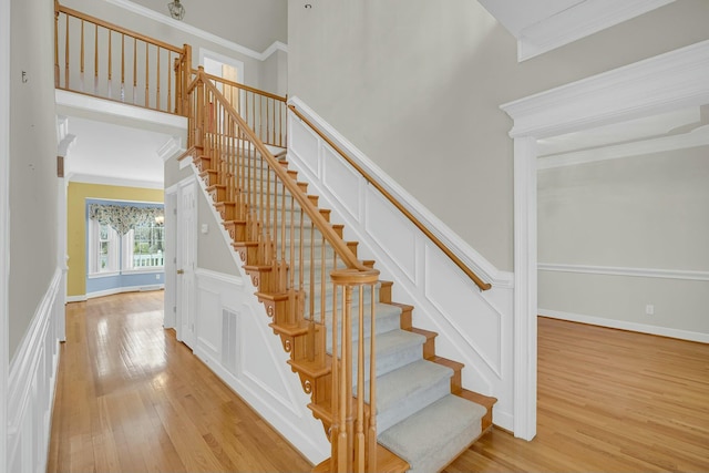 stairs featuring ornamental molding, a decorative wall, a towering ceiling, and wood finished floors