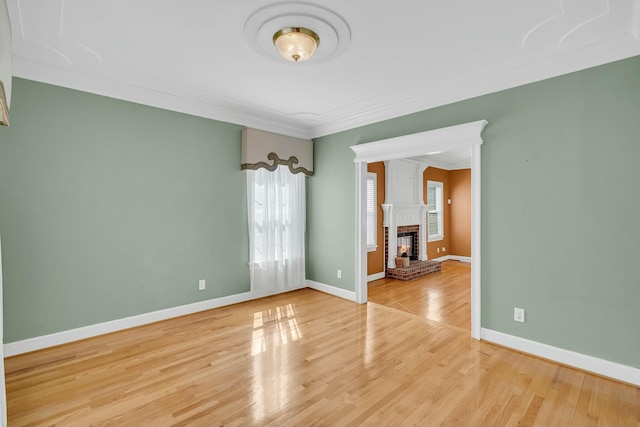 empty room featuring light wood finished floors, a brick fireplace, baseboards, and ornamental molding