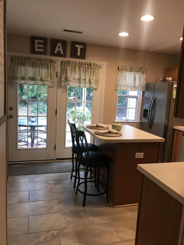 kitchen featuring a breakfast bar, a center island, stainless steel refrigerator with ice dispenser, light countertops, and visible vents