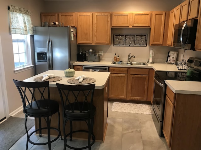 kitchen featuring a kitchen island, appliances with stainless steel finishes, a kitchen breakfast bar, light countertops, and a sink