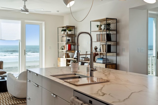 kitchen featuring a sink, a ceiling fan, stainless steel fridge, and light stone countertops