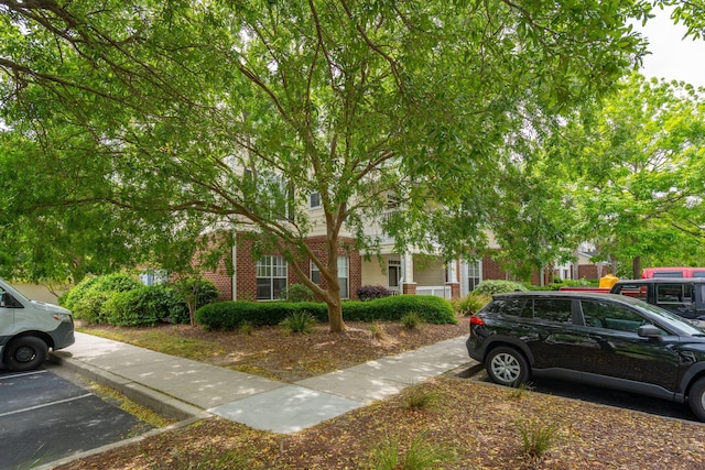 view of property hidden behind natural elements featuring brick siding and uncovered parking