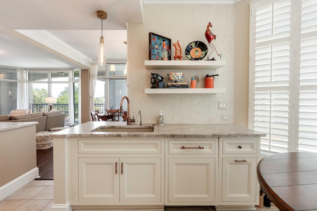kitchen featuring a sink, ornamental molding, open floor plan, pendant lighting, and light stone counters