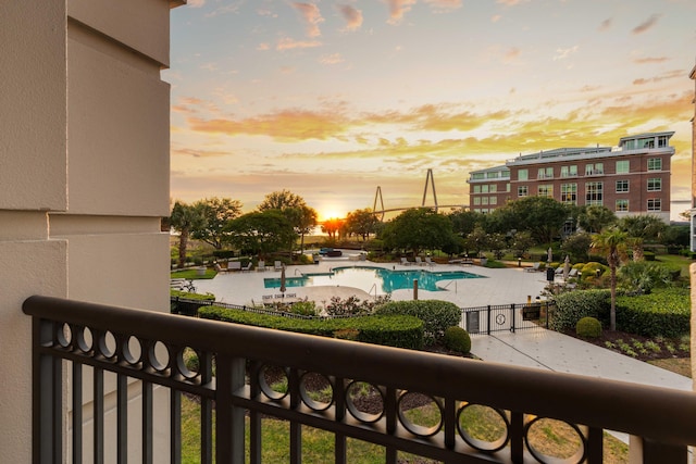balcony at dusk featuring view of pool and a patio