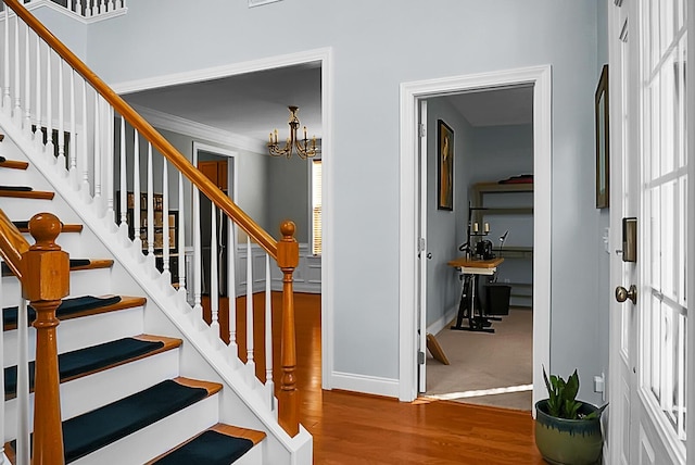 stairs with wood-type flooring, crown molding, and an inviting chandelier