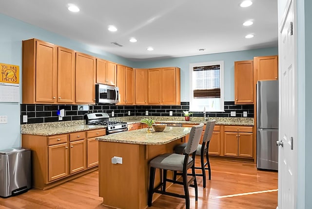 kitchen with light stone countertops, a center island, a kitchen breakfast bar, appliances with stainless steel finishes, and light wood-type flooring