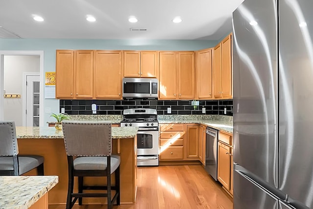 kitchen featuring backsplash, stainless steel appliances, light stone counters, and a breakfast bar area