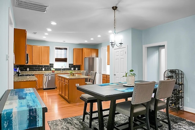 kitchen with pendant lighting, a center island, decorative backsplash, appliances with stainless steel finishes, and light hardwood / wood-style floors