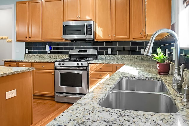 kitchen with sink, light stone counters, backsplash, appliances with stainless steel finishes, and light wood-type flooring