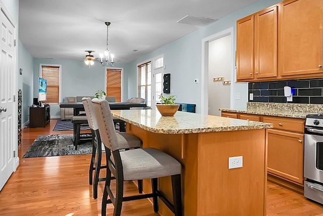 kitchen with tasteful backsplash, decorative light fixtures, an inviting chandelier, a center island, and light hardwood / wood-style floors