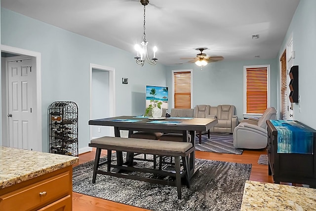 dining space with ceiling fan with notable chandelier and hardwood / wood-style flooring