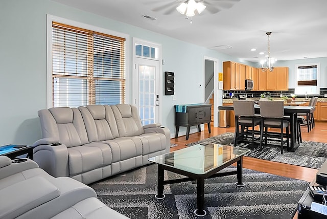 living room featuring ceiling fan with notable chandelier and light wood-type flooring