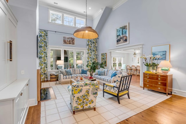 living area with a towering ceiling, light wood finished floors, baseboards, and ornamental molding