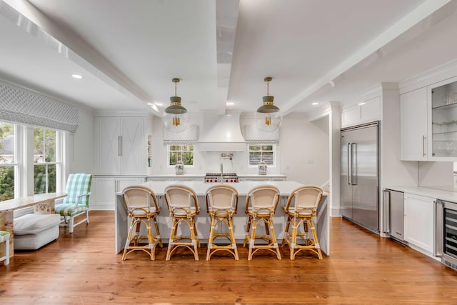 kitchen featuring a breakfast bar, light countertops, glass insert cabinets, white cabinetry, and stainless steel built in refrigerator