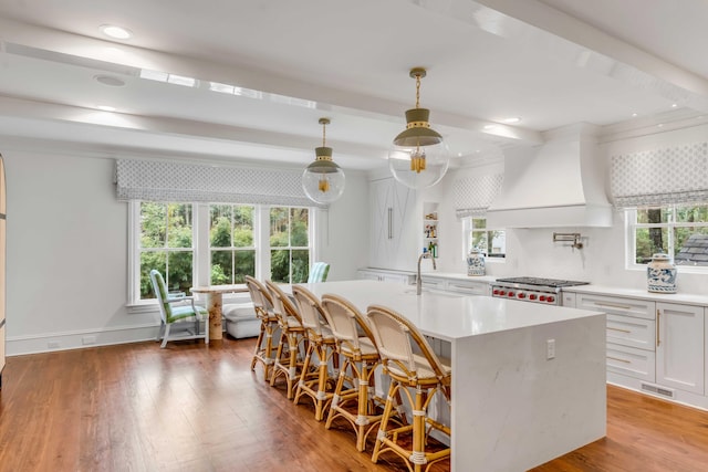 kitchen with premium range hood, white cabinetry, light countertops, a kitchen bar, and decorative light fixtures