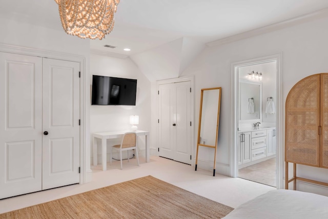 bedroom featuring two closets, lofted ceiling, light colored carpet, ensuite bathroom, and a sink