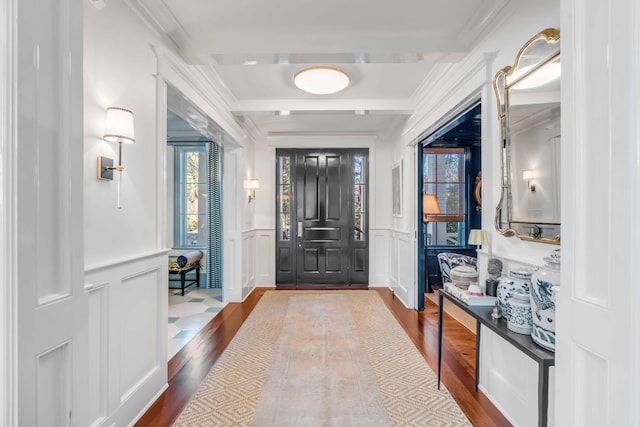 entryway featuring ornamental molding, wainscoting, wood finished floors, and a decorative wall