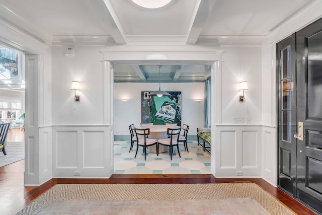 dining space with light wood-type flooring, a wainscoted wall, beamed ceiling, and a decorative wall