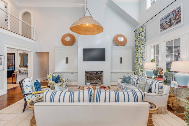 living room featuring a glass covered fireplace, crown molding, and a high ceiling