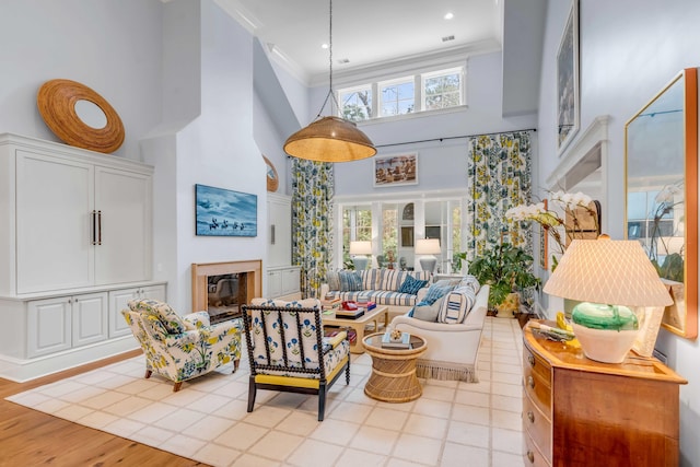 living room with ornamental molding, a glass covered fireplace, a towering ceiling, and light wood finished floors