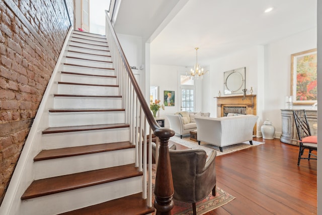 staircase with a chandelier, brick wall, and hardwood / wood-style flooring