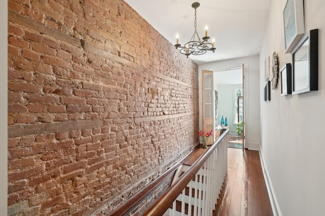 corridor with dark hardwood / wood-style floors, an inviting chandelier, and brick wall