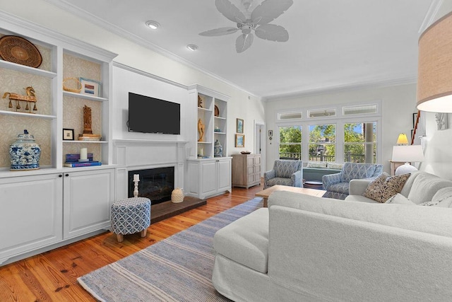 3052 Seabrook Island Rd, Seabrook Island, SC 29455 - living room featuring crown molding, light wood-style flooring, ceiling fan, a glass covered fireplace, and built in shelves