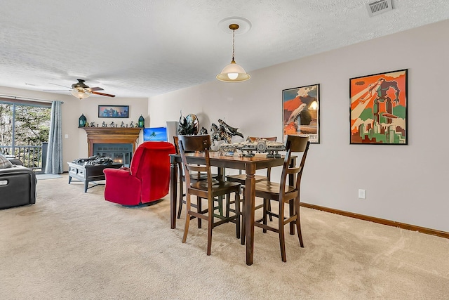 carpeted dining area with a glass covered fireplace, visible vents, a textured ceiling, and baseboards