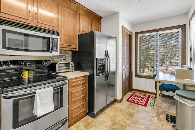 kitchen featuring a toaster, baseboards, brown cabinetry, decorative backsplash, and appliances with stainless steel finishes