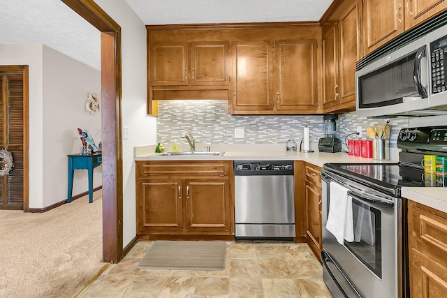 kitchen featuring stainless steel appliances, a sink, light countertops, and brown cabinets