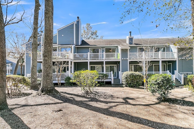 rear view of house with covered porch, a chimney, and a balcony