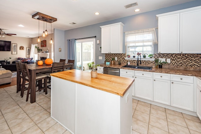 kitchen featuring sink, butcher block counters, a center island, decorative light fixtures, and white cabinets