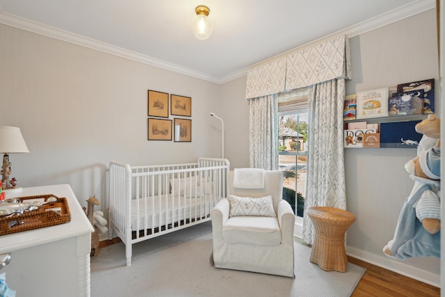 bedroom with a nursery area, ornamental molding, and hardwood / wood-style flooring