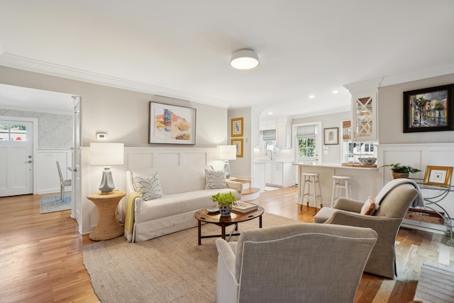 living room with ornamental molding, sink, and light wood-type flooring