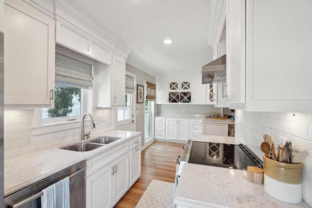 kitchen featuring wall chimney exhaust hood, sink, white cabinetry, light stone counters, and stainless steel appliances