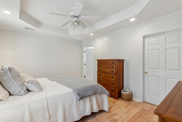 bedroom with a tray ceiling, light wood-style flooring, and crown molding