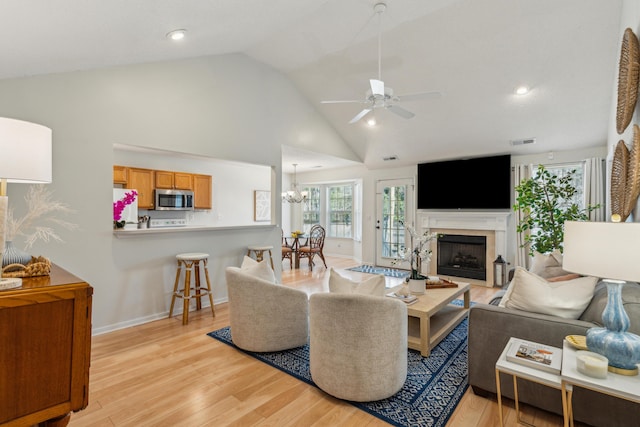 living area featuring visible vents, baseboards, light wood-style flooring, a fireplace, and ceiling fan with notable chandelier