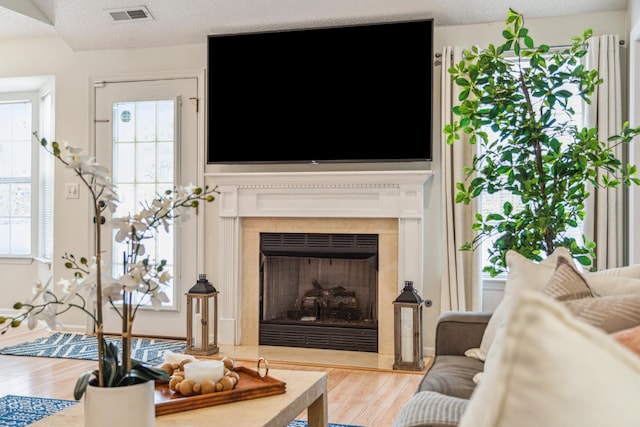 living room featuring a fireplace, plenty of natural light, wood finished floors, and visible vents