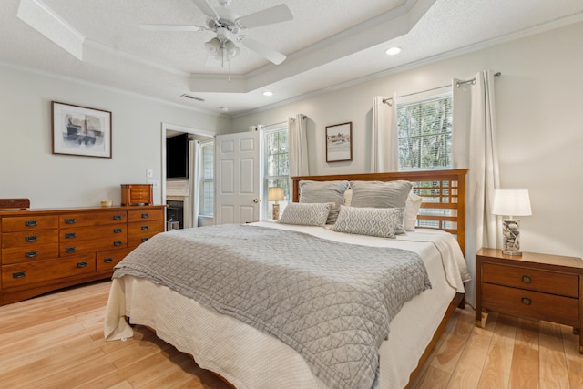 bedroom with a tray ceiling, multiple windows, light wood-style floors, and crown molding