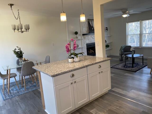 kitchen with white cabinetry, decorative light fixtures, light stone countertops, ceiling fan with notable chandelier, and a tile fireplace