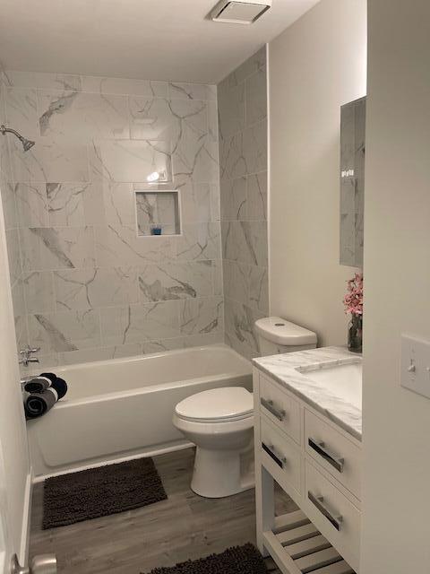 full bathroom with toilet, tiled shower / bath, wood-type flooring, and vanity