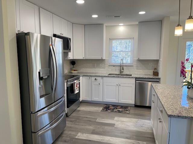 kitchen featuring pendant lighting, white cabinetry, stainless steel appliances, sink, and light stone counters