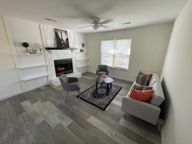 living room with ceiling fan, wood-type flooring, and a stone fireplace