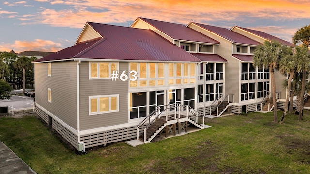 rear view of property with metal roof, a lawn, stairs, and a sunroom