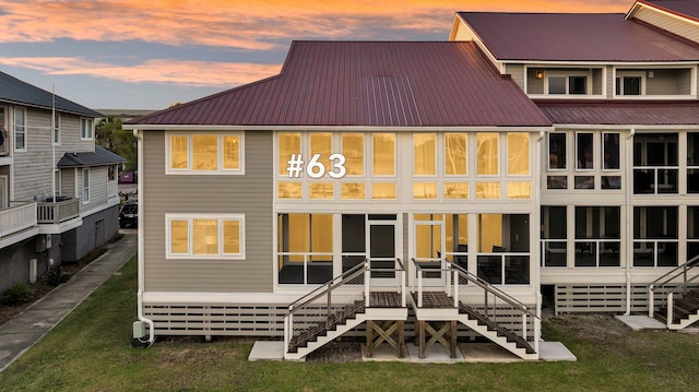 back of house at dusk featuring stairs, metal roof, and a yard
