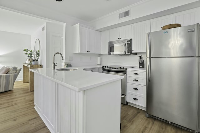 kitchen featuring stainless steel appliances, a sink, white cabinets, light countertops, and ornamental molding