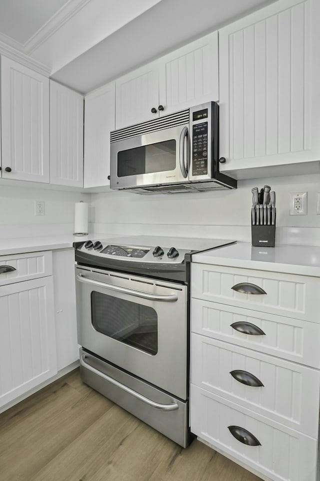 kitchen with stainless steel appliances, white cabinetry, light countertops, ornamental molding, and light wood finished floors